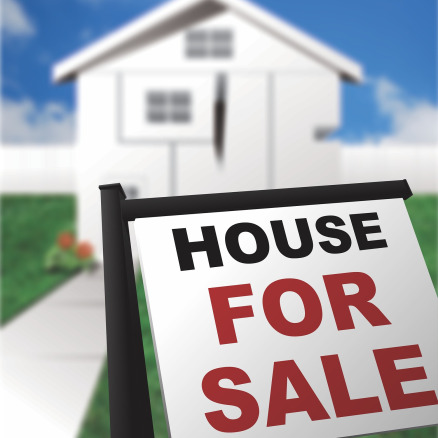 A white colored house with a "house for sale" sign in front
